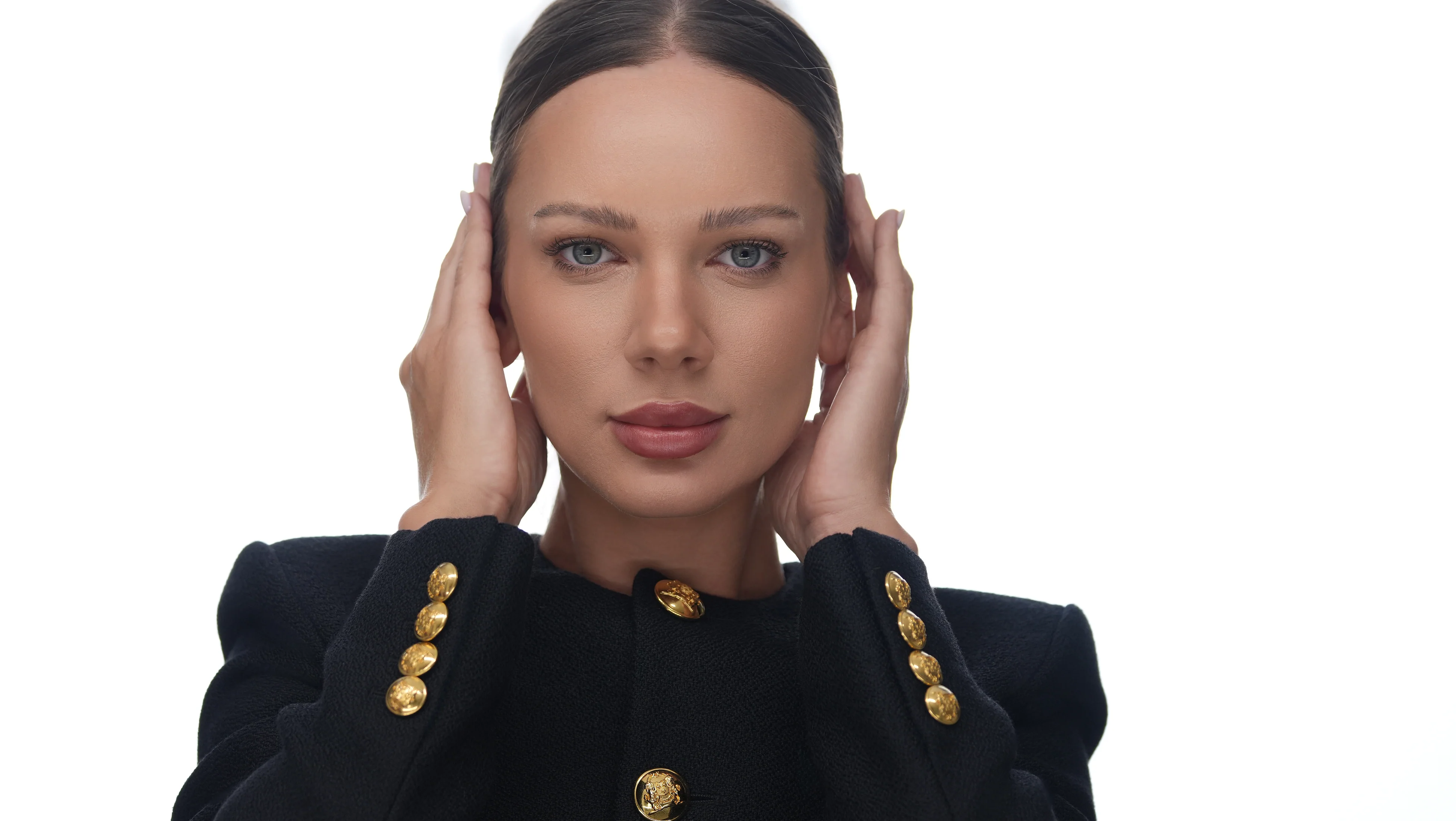 Roxana Diaconu with her hands at her temples, in a black jacket with gold buttons.